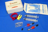 A set of bicycle brake bleed kit components including adapters, syringes, a block with tubing, a Valcro tie, gloves, and O-rings, primarily in yellow, red, and clear colors, displayed next to its packaging box.