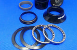 A set of black FSA bicycle threadless headset components laid out on a blue background, including a top cap with bolt, spacers, a top cover, ball bearings, a compression ring, and seals.