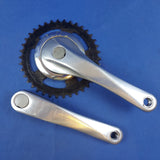 A vintage silver bicycle crankset with chainring, viewed from the top and side, on a blue background.